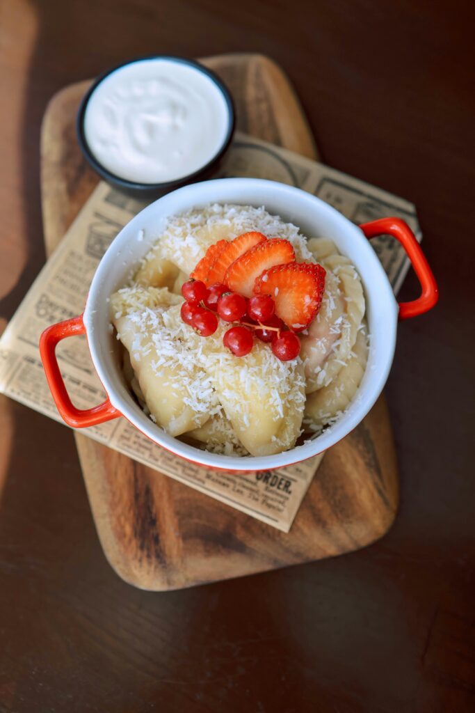 Delicious fruit-topped dumplings with coconut shreds in a red bowl on a wooden cutting board.