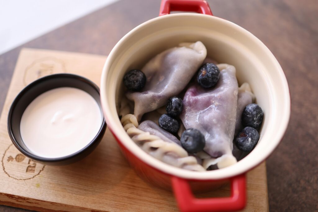 Tastefully arranged blueberry dumplings with a side of cream in a ceramic pot.