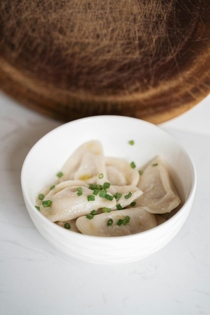 A bowl of fresh uncooked dumplings garnished with green chives, ready for cooking.